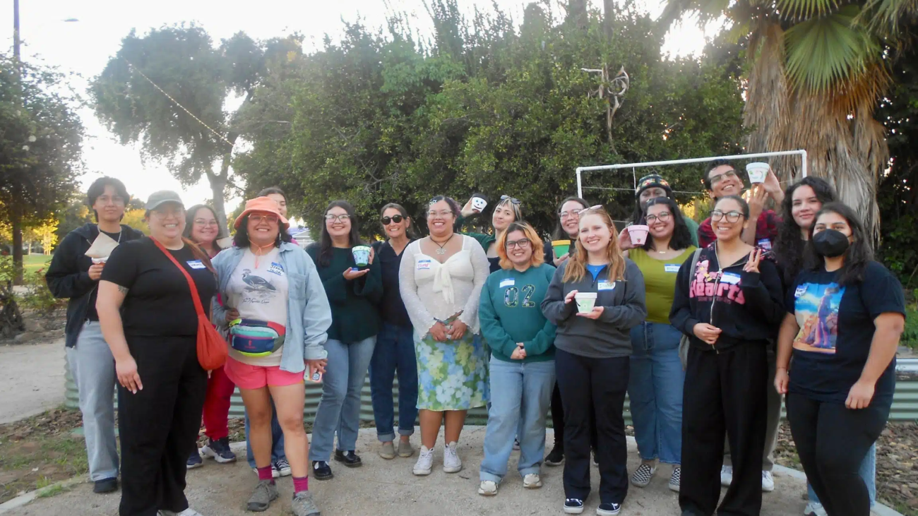a group of 20 mostly young people holding personalized plant potters in a garden